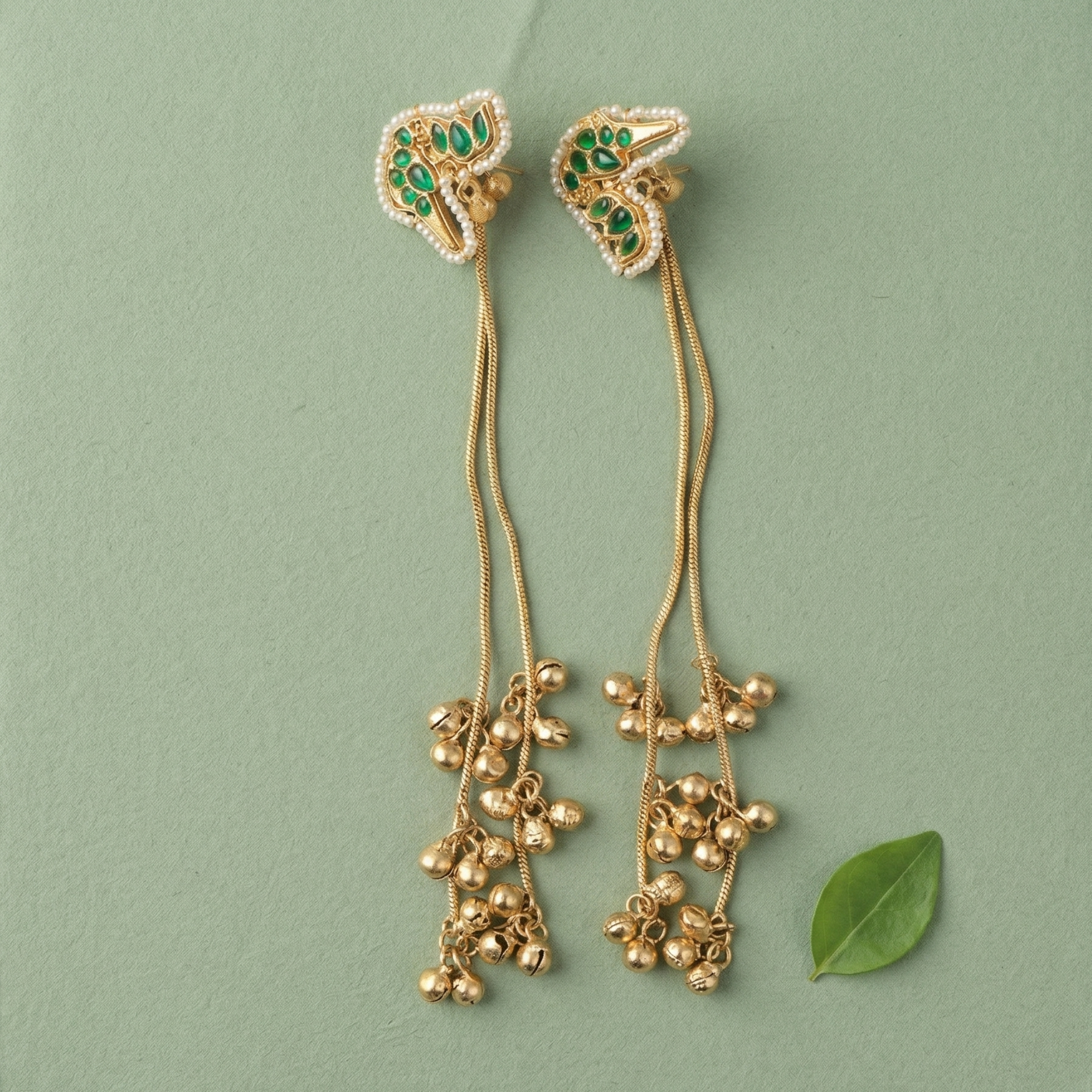 Yugavi Jhankaar Emerald peacock ghungroo drop earrings in bright gold finish — all-emerald green peacock stud outlined in seed pearls with three gold chain drops ending in ghungroo bell clusters, displayed as a pair