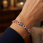 Rose gold bracelet with blue evil eye beads on a wrist against a blurred background