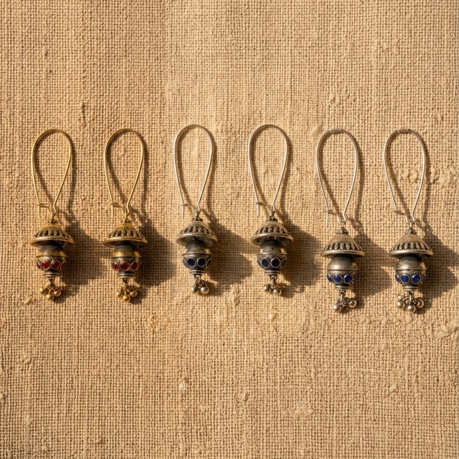 Five matching antique-style metal pendant earrings with loop tops and dangling clover-shaped charms, arranged in a row on a textured beige fabric background.