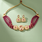 Gold-plated Indian jewelry set featuring a multi-strand necklace with deep magenta beaded strands and three central decorative gold medallions, accompanied by matching drop earrings, displayed on a soft sage green background.