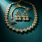 Gold-tone Indian kumkum jewelry set including a necklace and matching earrings, featuring small teardrop-shaped stones with green enamel borders and colorful beaded tassels, displayed on a dark teal velvet surface.