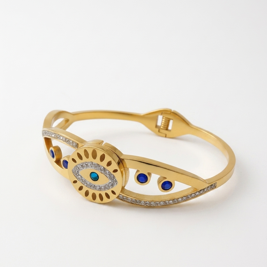 Gold-tone hinged bangle bracelet featuring an evil eye motif with blue and white stones, accented with small blue and white stones along the band, shown on a clean white background.