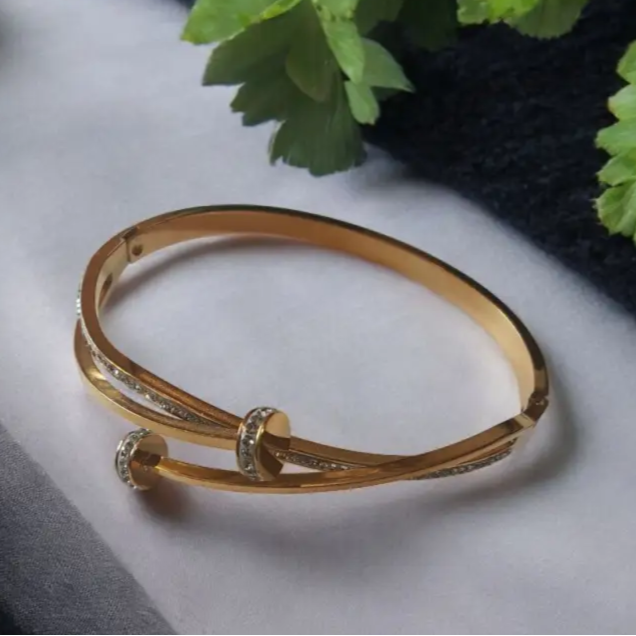 Gold bracelet on a white surface with green leaves in the background