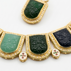 Gold-tone necklace with rectangular carved stone panels in green, teal, and black, accented with small red and green stones, on a white background.