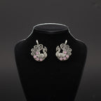 Silver earrings with pink stones on a black stand against a dark background