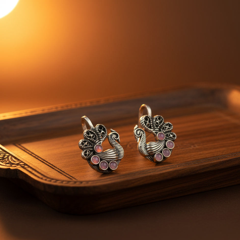 Pair of silver earrings with pink gemstones on a wooden surface