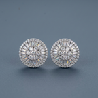 A pair of round silver-toned stud earrings with intricate halo and baguette crystal detailing, displayed on a dark slate gray background.
