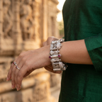 Overhead view of Yugavi Prasada wide silver temple bracelet forming a complete circle — eight hinged temple-module links with dome tops, arched gateways, devotional figure panels and ruby red cabochon accents visible across the band