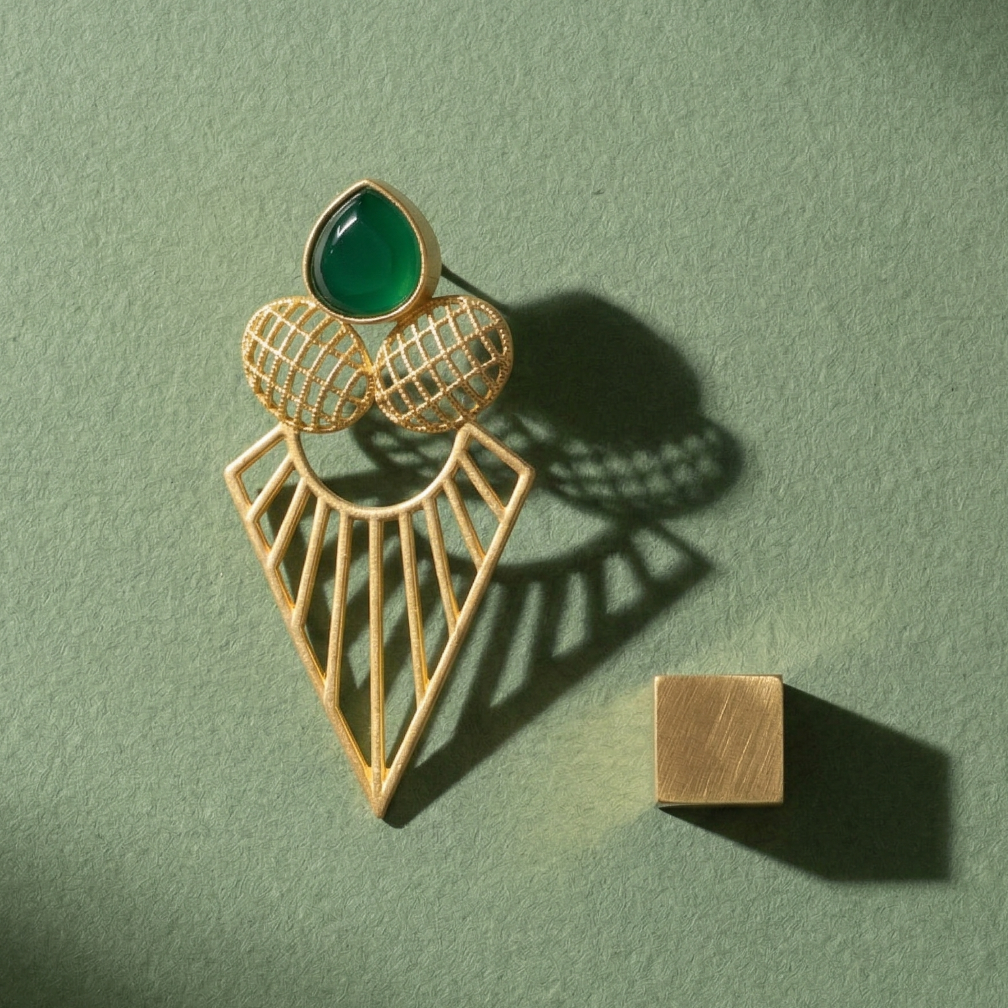 Side profile of Yugavi Kirana geometric earring showing full length — emerald teardrop stud at top, cross-hatched grid ovals, and wide open-work gold triangle arrow-pointed drop below, demonstrating the architectural scale of the piece