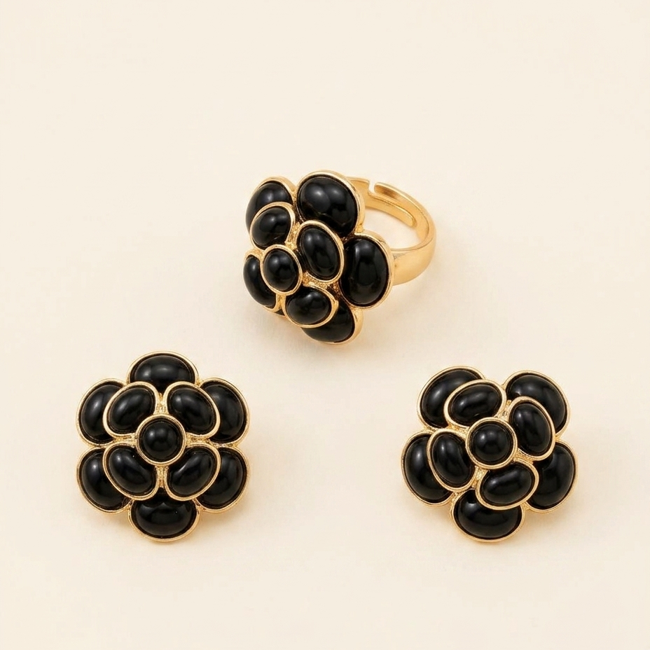 Three-piece gold jewelry set featuring a ring and matching stud earrings, each designed with a cluster of black oval stones set in gold-tone metal, displayed on a warm cream background.