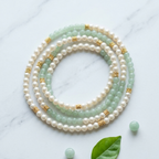 Three beaded bracelets arranged in concentric circles on a white marble surface. The bracelets feature white pearls, light green jade-like beads, and small gold star-shaped spacers.