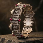 Woman's wrist wearing the Yugavi Prasada wide oxidised silver temple architecture bracelet — showing the full band of hinged temple modules with shikhara domes, ruby stones and torana arches against a draped silk fabric background