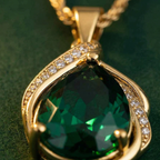 Woman wearing Yugavi Tarang gold emerald pendant necklace — faceted green teardrop stone in gold pavé wave frame on twisted rope chain at collarbone, styled for an evening dinner or festive occasion