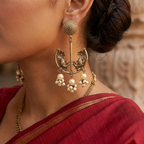 Yugavi Bhavika antique gold peacock chandbali pearl drop earrings displayed as a pair on white background — sunburst disc stud, slender bar connector, wide crescent chandbali with mirrored peacock open-work engraving and star flower motif, large central pearl with seed pearl cluster fringe, antique gold finish, House of Yugavi Kansyam Collection