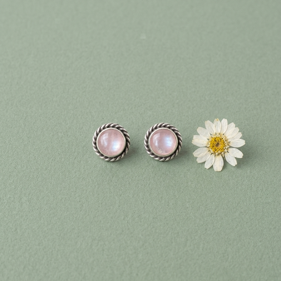 Yugavi Bindu minimalist silver stud earrings — round white moonstone or mother of pearl cabochon in twisted rope silver bezel setting, push-back stud closure, displayed as a pair on taupe fabric