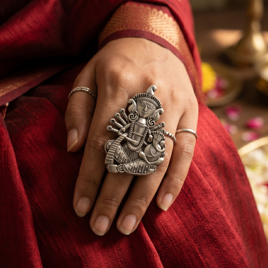 Hand wearing a decorative silver ring with a red saree background