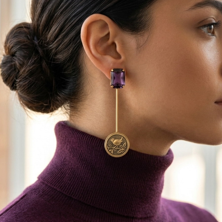 Woman wearing a gold earring with a purple gemstone, looking to the side.