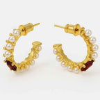 Yugavi Ishira gold pearl hoop earrings on grey stone surface with red rose petals — C-hoop pair showing hammered gold band with seed pearls individually set along the full outer arc, push-back stud closure, gold finish, lifestyle jewellery photography