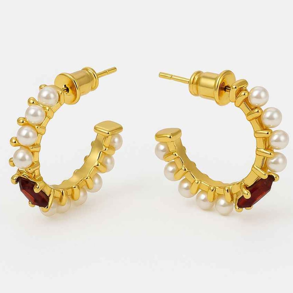 Yugavi Ishira gold pearl hoop earrings on grey stone surface with red rose petals — C-hoop pair showing hammered gold band with seed pearls individually set along the full outer arc, push-back stud closure, gold finish, lifestyle jewellery photography