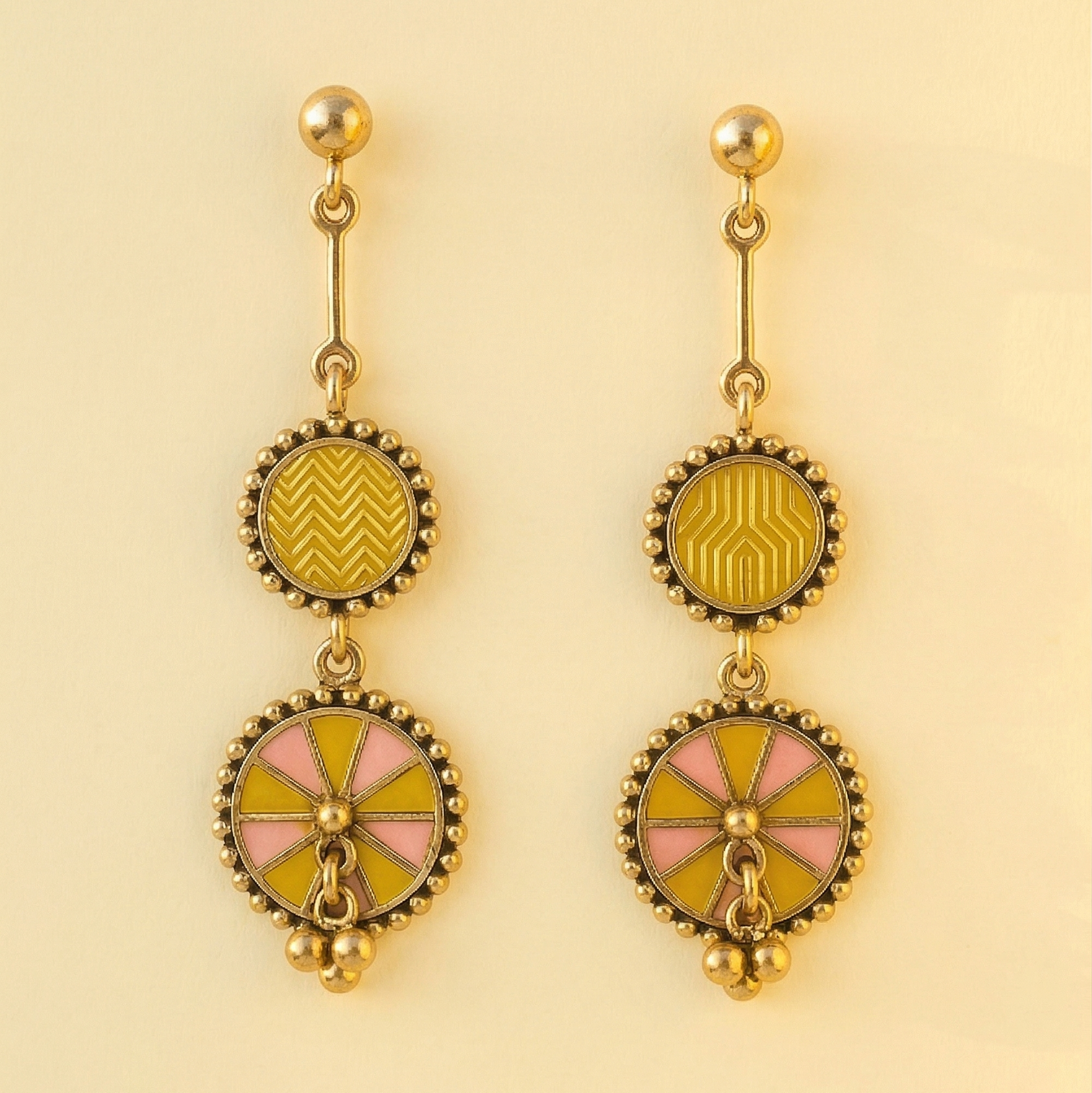 Yugavi Ishnavi double disc drop earrings displayed as a pair on off-white background — polished gold ball stud tops with bar connectors, medium circular upper discs with mustard yellow geometric enamel and gold bead borders, larger lower chakra wheel discs alternating mustard yellow and blush pink wedge enamel with central gold dome and three gold ball drops at base