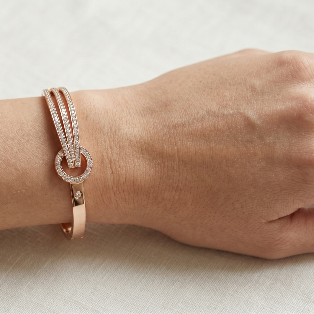 Yugavi Ishvini rose gold rigid bangle on white background — wide front face with three parallel channels of dense continuous pavé CZ crystal rails converging through a circular rose gold knot ring with partial pavé upper arc, single CZ stud accent, box hinge clasp visible at back