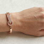 Yugavi Ishvini rose gold rigid bangle on white background — wide front face with three parallel channels of dense continuous pavé CZ crystal rails converging through a circular rose gold knot ring with partial pavé upper arc, single CZ stud accent, box hinge clasp visible at back