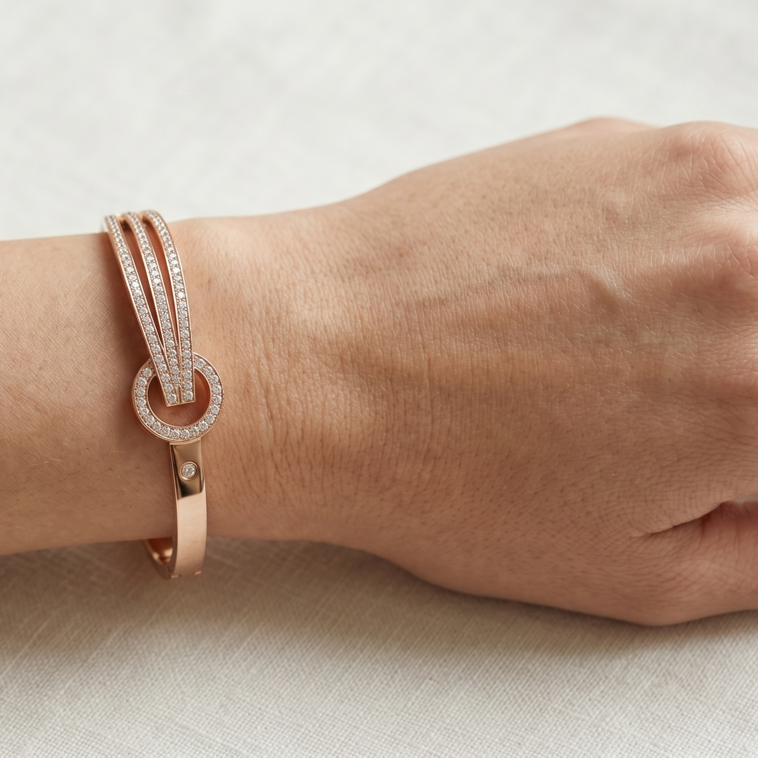 Yugavi Ishvini rose gold rigid bangle on white background — wide front face with three parallel channels of dense continuous pavé CZ crystal rails converging through a circular rose gold knot ring with partial pavé upper arc, single CZ stud accent, box hinge clasp visible at back
