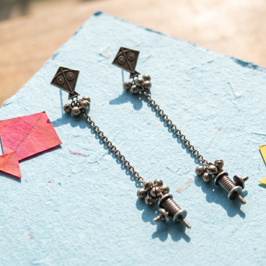Pair of earrings with chain and screw design on a blue surface with colorful paper shapes.