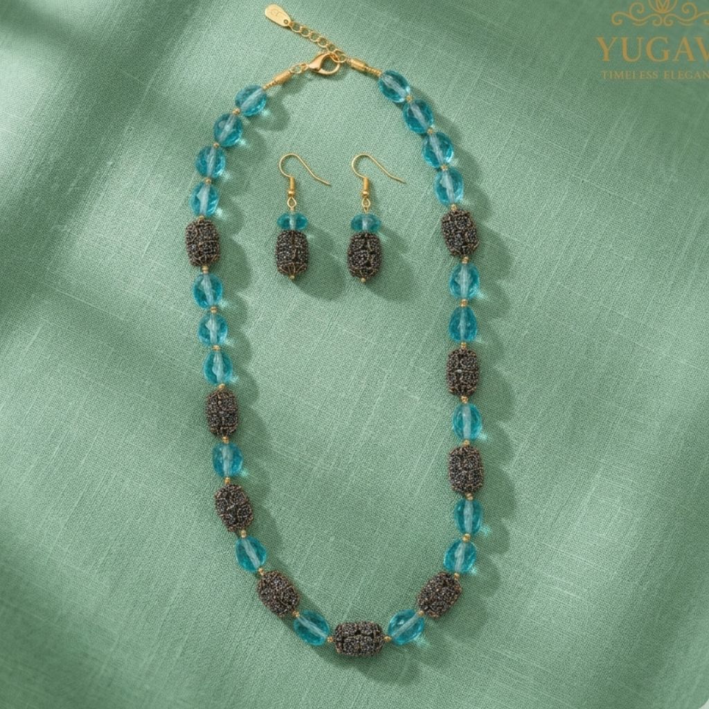 Jewelry set with necklace and earrings on a green fabric background, featuring the brand 'Yugavi'.