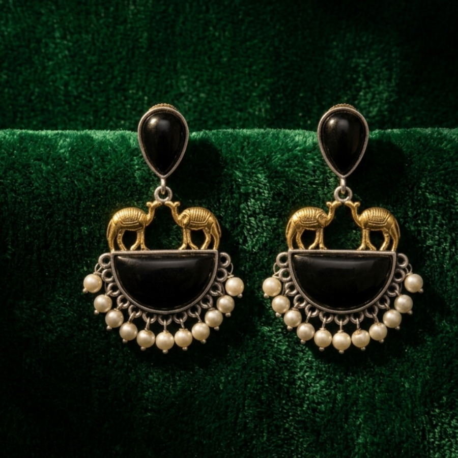 Yugavi Nevara dual metal camel black stone pearl fringe drop earrings on white background — black teardrop stone cabochon stud in oxidised silver bezel, two miniature antique gold camel sculptures facing each other atop a semicircular oxidised silver pendant with black stone inlay and pearl fringe, nine ivory pearl drops along the lower arc, House of Yugavi Kansyam Rajat Collection