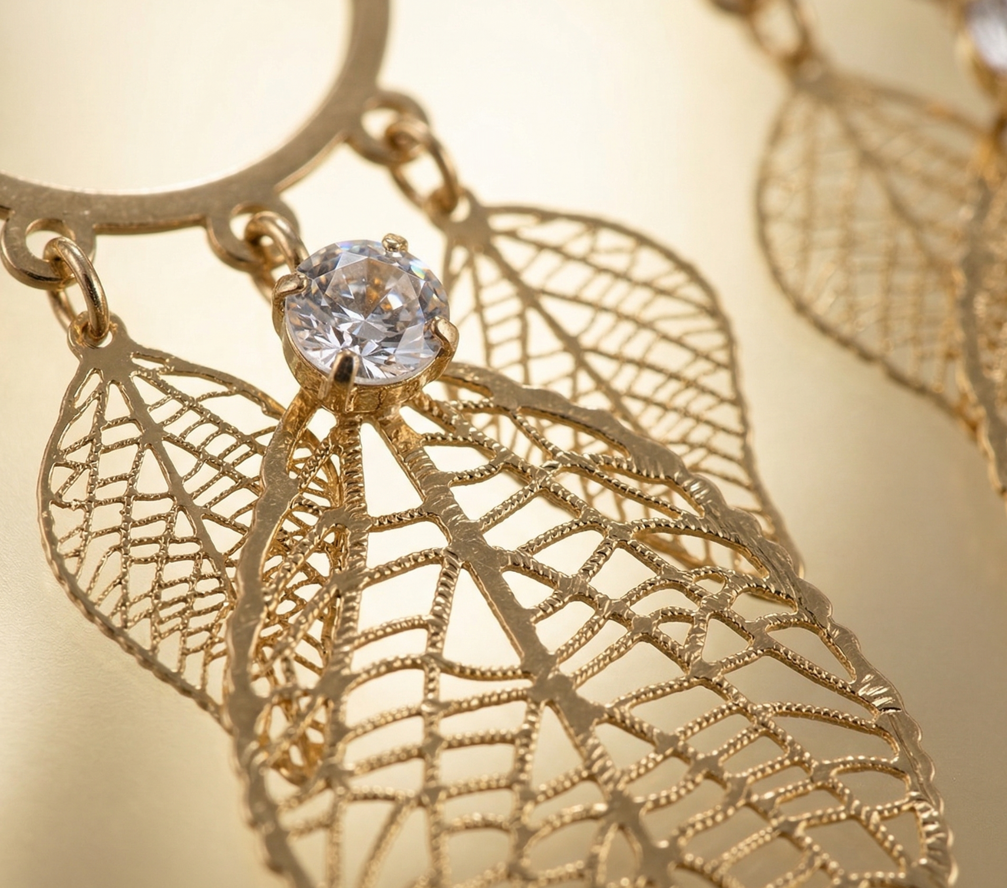 Gold leaf-shaped earring with a clear gemstone on a gold background