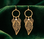 Gold leaf-shaped earrings with circular tops on a green velvet background