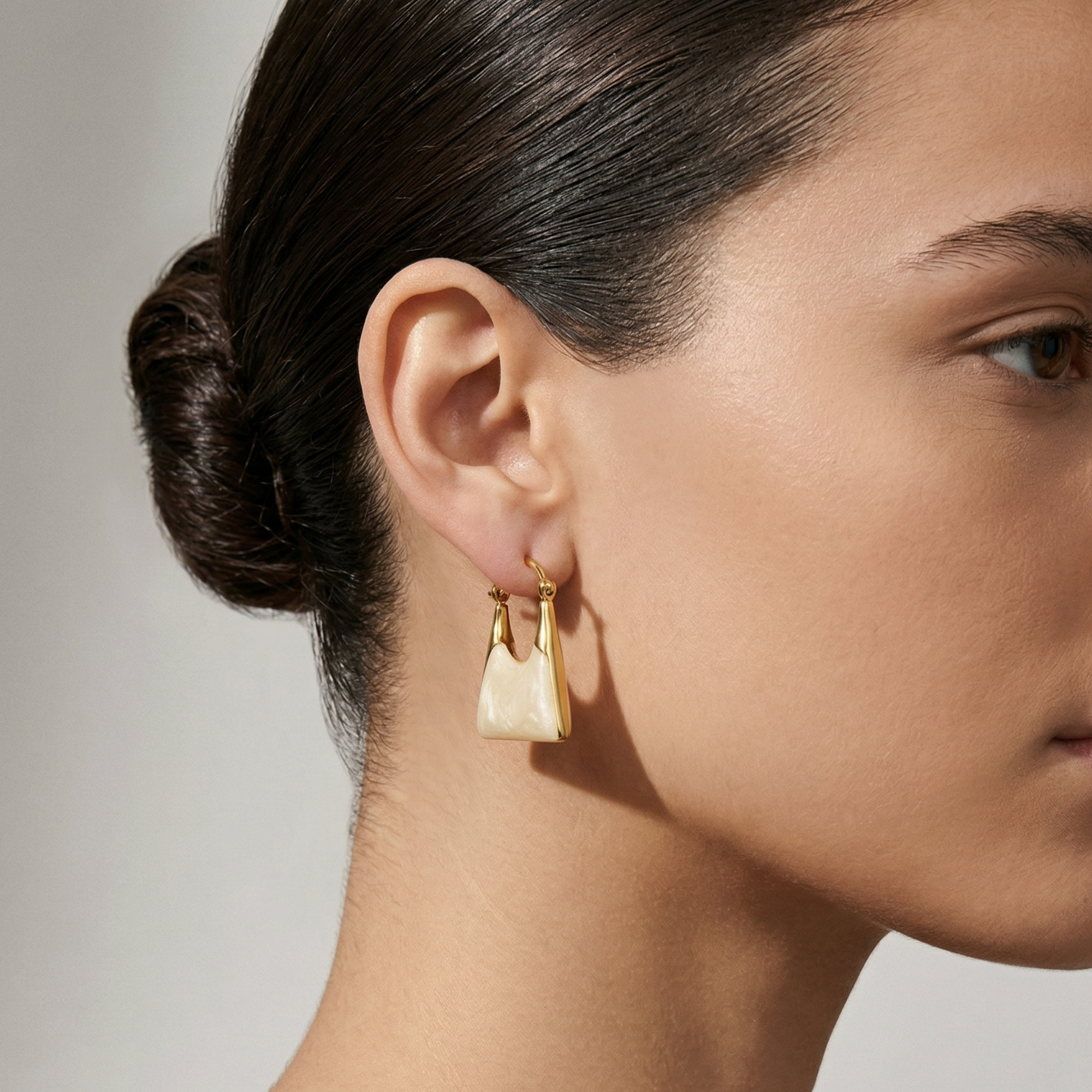 Close-up of a woman wearing gold earrings with a neutral background