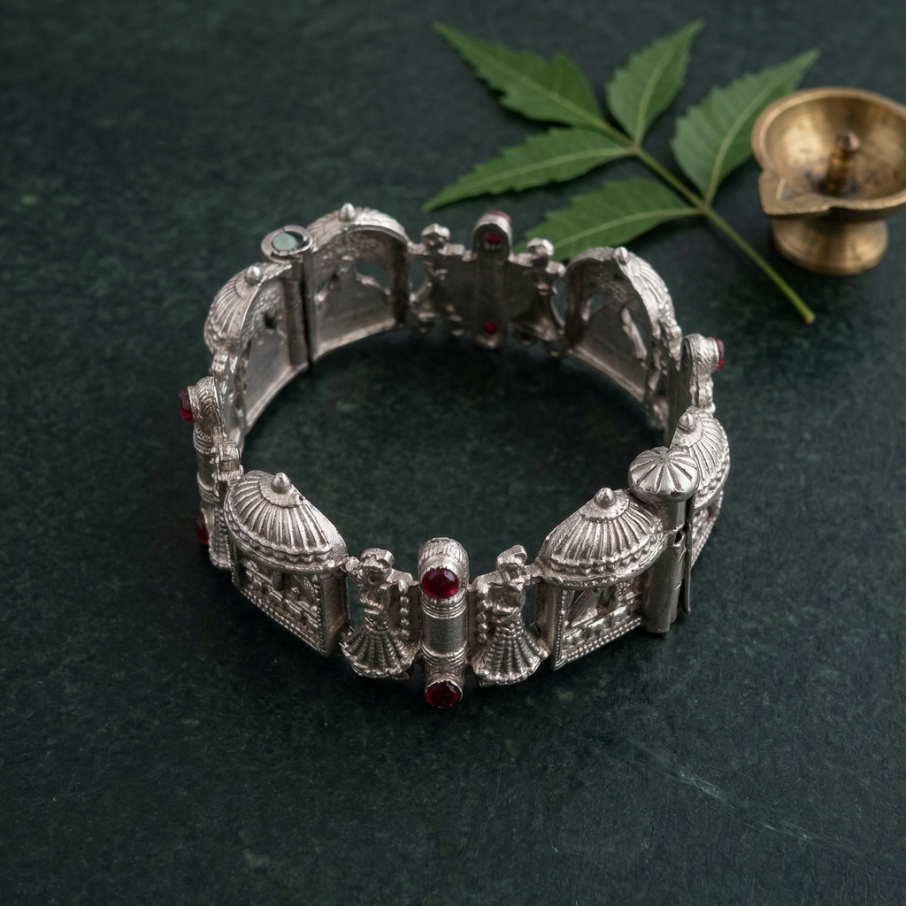 Yugavi Prasada temple architecture silver statement bracelet — top angled view showing eight hinged links each with a ribbed dome shikhara finial and open torana arched gateway panels, ruby red cabochon stones at hinge joints, oxidised silver finish