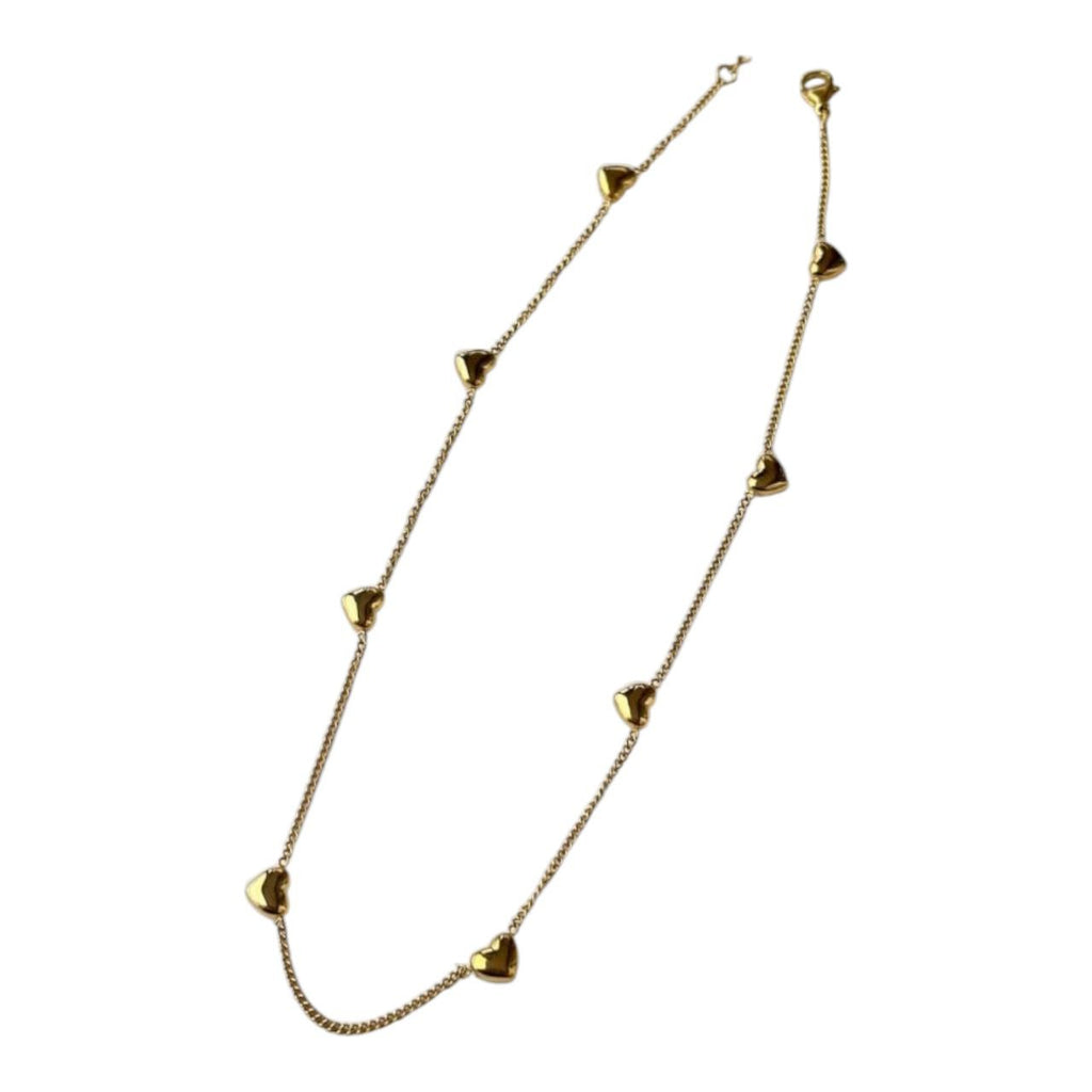 Yugavi Saisha gold multi-heart station necklace worn at collarbone — delicate gold cable chain with multiple small puffy 3D gold hearts evenly spaced along full length, shown on model in beige shirt collar, bright gold finish