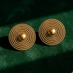 Yugavi Sejal large gold circular disc stud earrings displayed as a pair on white background — concentric rings of fine rope-twist gold texture radiating outward from a central raised polished dome, antique gold finish showing depth and shadow in the ring recesses