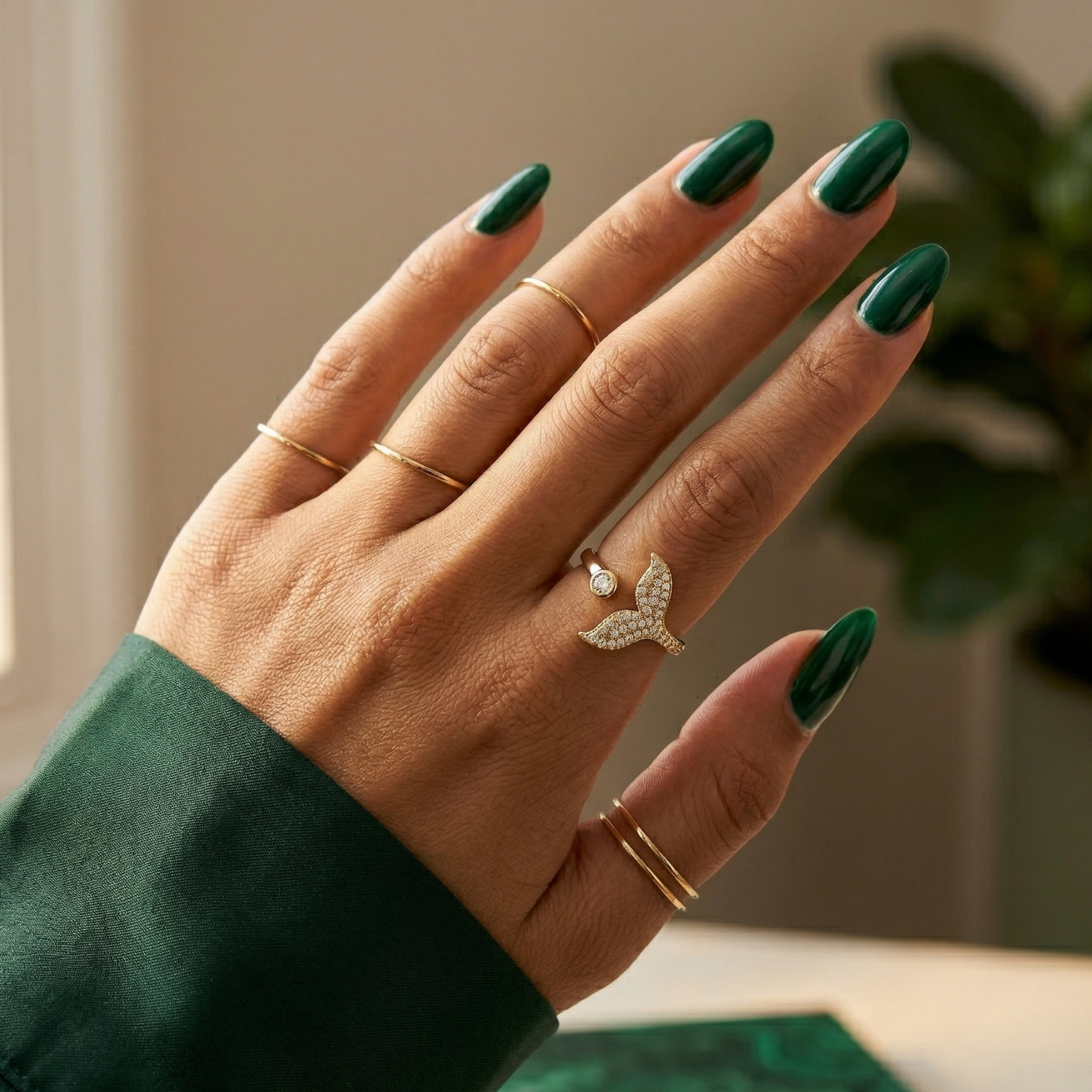 Hand with green nail polish wearing multiple rings against a neutral background
