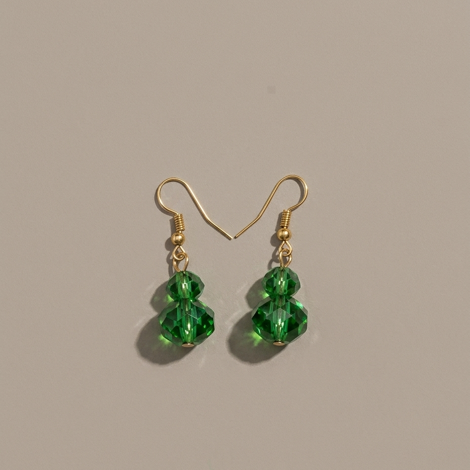 A pair of gold-tone dangle earrings with three faceted green crystal beads hanging from each hook, displayed on a neutral beige background.