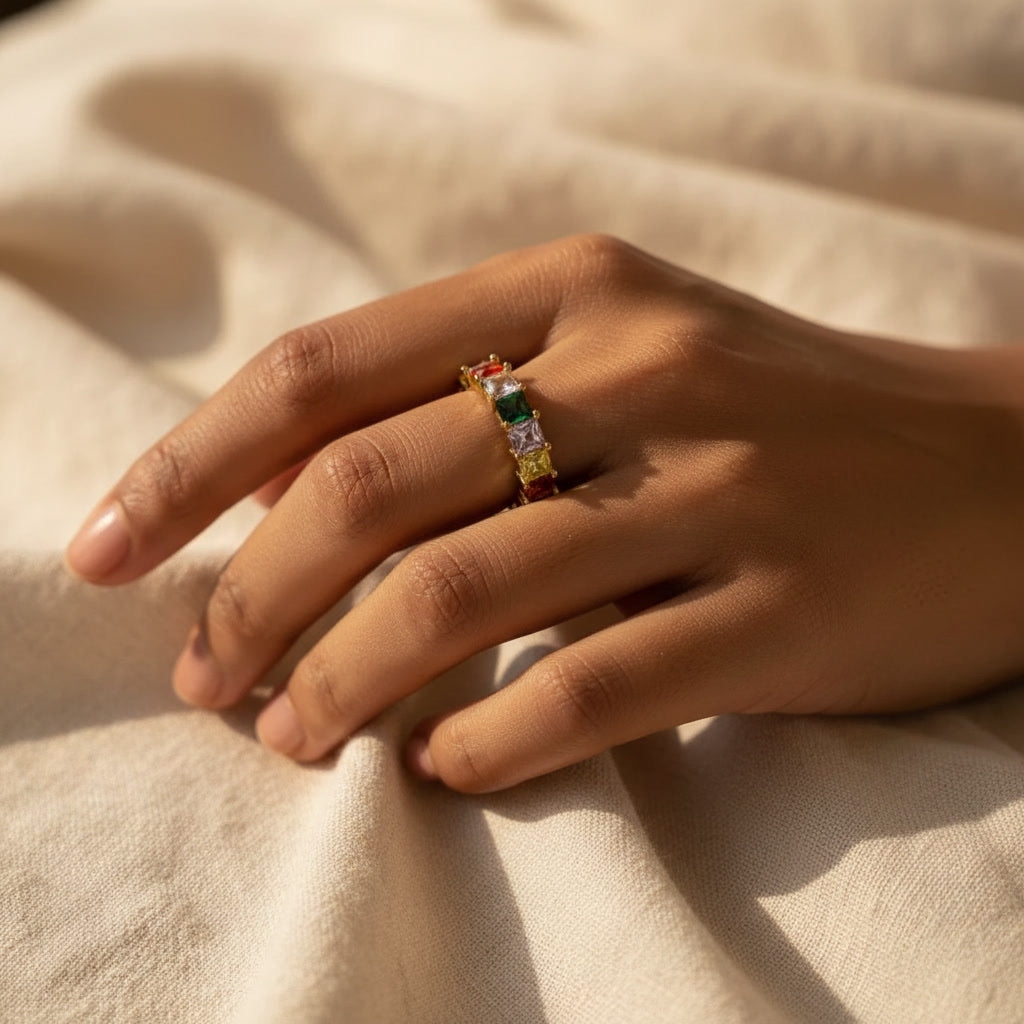 Hand wearing a ring with colorful gemstones on a beige fabric background