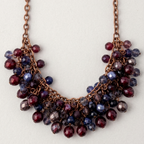 A copper-toned chain necklace with a dense, tiered cluster of faceted beads in deep burgundy and navy blue, displayed against a light off-white background.