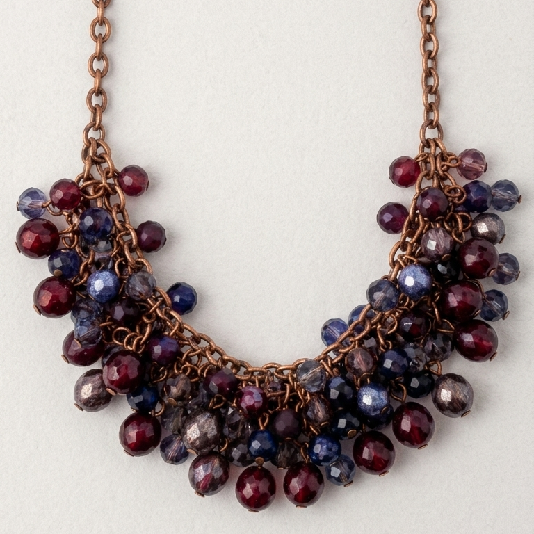 A copper-toned chain necklace with a dense, tiered cluster of faceted beads in deep burgundy and navy blue, displayed against a light off-white background.